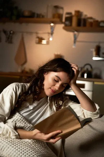 A beautiful young woman reads intently on her couch, immersed in the warmth of her home. — Stock Photo
