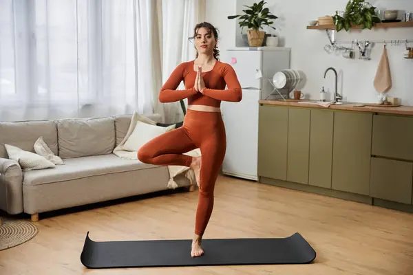 Una joven con gracia se equilibra en una pierna, practicando yoga en el interior en paz. - foto de stock