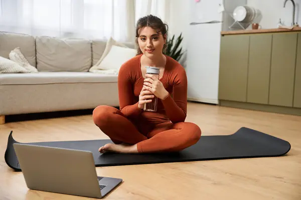 A young woman seated comfortably at home enjoys her warm drink while connecting online. — Stock Photo