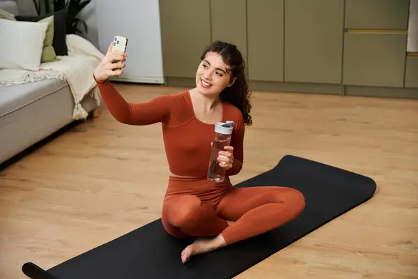 Bright and cheerful young woman captures a fun selfie while relaxing on her yoga mat. — Stock Photo