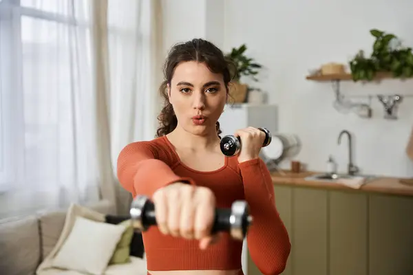 Ejercitando en casa, esta joven muestra su fuerza y determinación mientras levanta pesas. - foto de stock