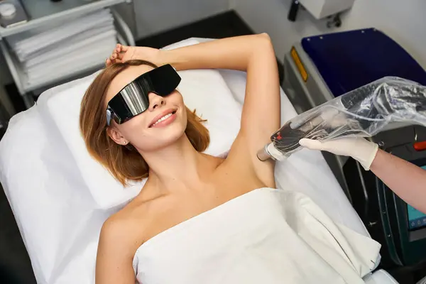 A beautiful young woman is smiling while getting a laser hair removal treatment in a sleek clinic. — Stock Photo