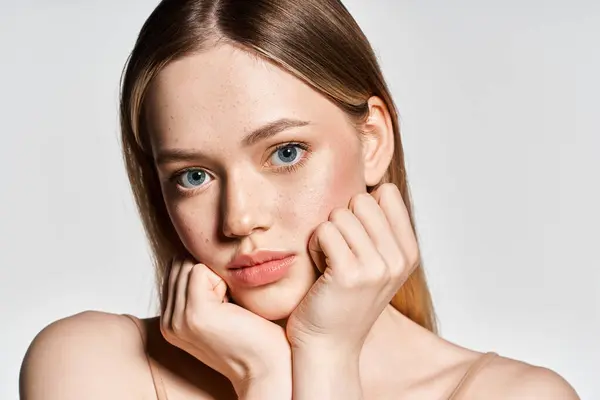 Young woman with striking blue eyes poses gracefully with hands near her face in soft light — Stock Photo
