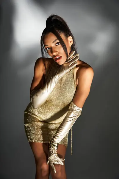 Elegance and allure of a stylish young woman dressed in shimmering gold attire at a photoshoot. — Stock Photo