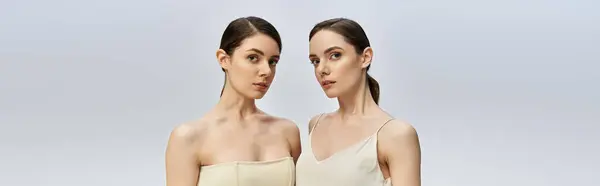 Two charming twin sisters stand side by side in a minimalist setting, radiating confidence. — Stock Photo