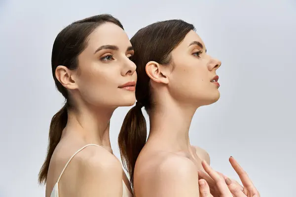 Two beautiful twin sisters pose back to back, highlighting their elegant features and bond. — Stock Photo