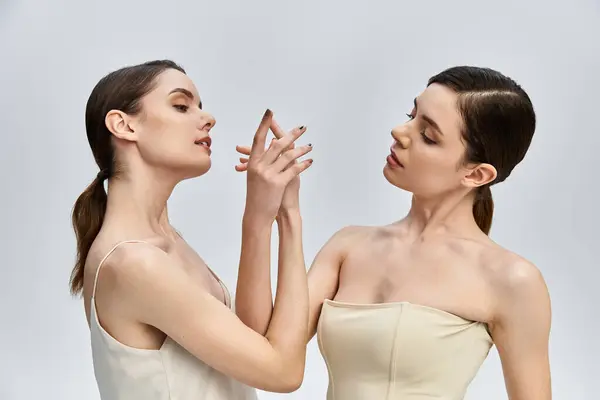 Two beautiful twin sisters gracefully touch each other hands in a serene environment. — Stock Photo