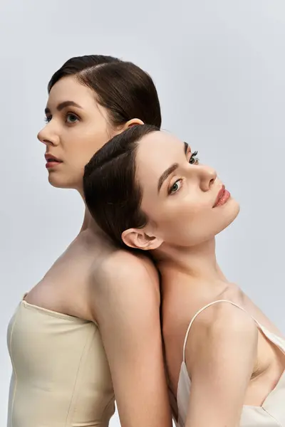 Twins embody beauty and poise as they stand back to back with enchanting gazes. — Photo de stock