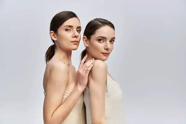 Two beautiful twin sisters pose close together in a soft, neutral toned studio, radiating charm. — Stock Photo