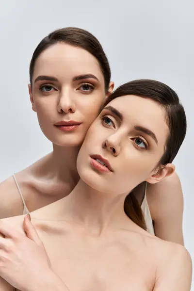 Two stunning twin sisters exhibit elegance and poise in a minimalist backdrop, radiating warmth. — Stock Photo