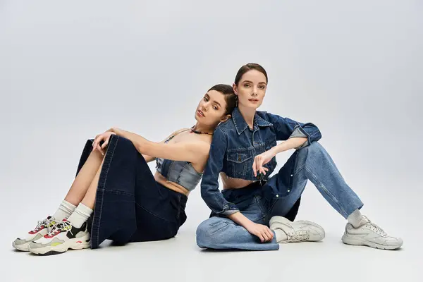 Two beautiful sisters sit comfortably on the floor, radiating confidence and style. — Stock Photo