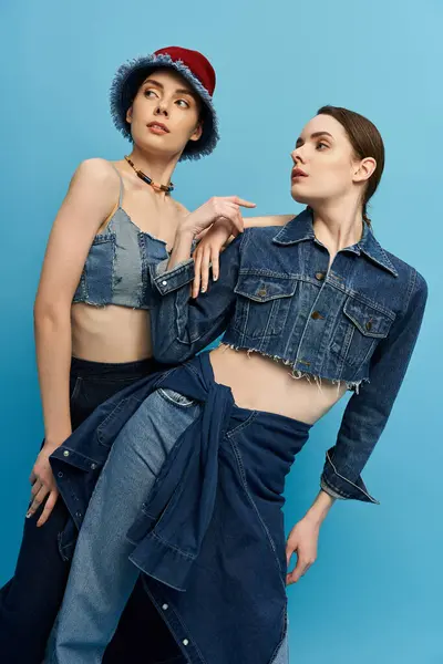 Twins showcase their unique style and confidence against a vibrant blue wall. — Stock Photo