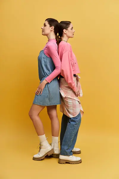 Two beautiful twin sisters stand back to back, wearing stylish outfits and exuding confidence. — Stock Photo