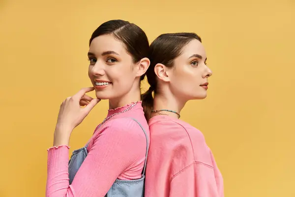 Beautiful sisters pose back to back, sharing joyful smiles in a cheerful setting. — Stock Photo