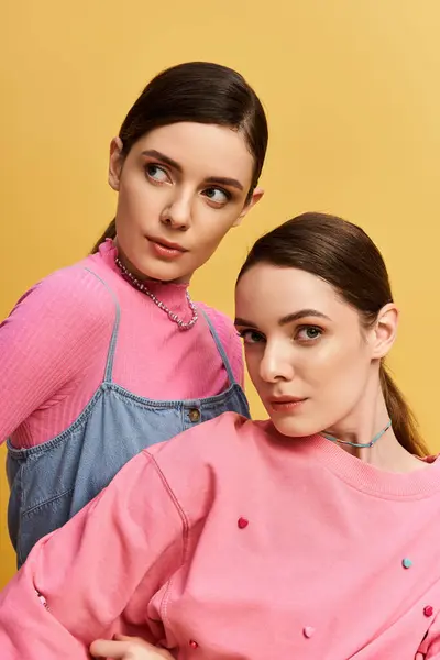 Dos hermosas hermanas gemelas muestran su estilo, irradiando encanto sobre un fondo amarillo brillante. - foto de stock