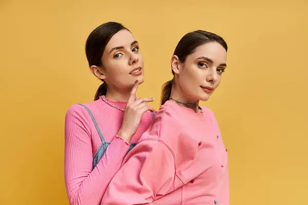 Two beautiful sisters stand back to back, playfully posing in bright pink outfits, radiating joy. — Stock Photo
