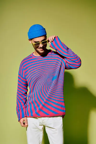 A handsome young man wears a colorful outfit while posing playfully against a green backdrop. — Stock Photo