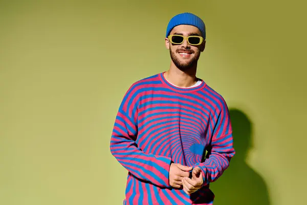 A stylish young man displays his trendy outfit and bold sunglasses against a green backdrop. — Stock Photo