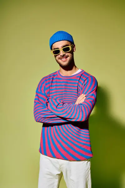 Handsome young man confidently displays his trendy outfit and sunglasses against green backdrop. — Stock Photo
