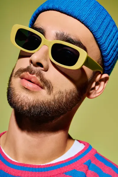A young man exudes confidence in a stylish outfit and trendy sunglasses against a green backdrop. — Stock Photo