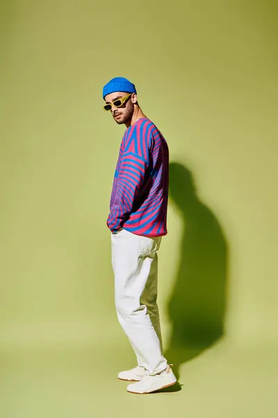 A young man displays his style in trendy sunglasses and a colorful outfit in a studio. — Stock Photo