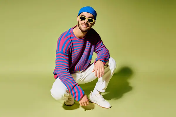 A handsome young man wearing colorful sunglasses and a striped sweater strikes a pose in a studio. — Stock Photo