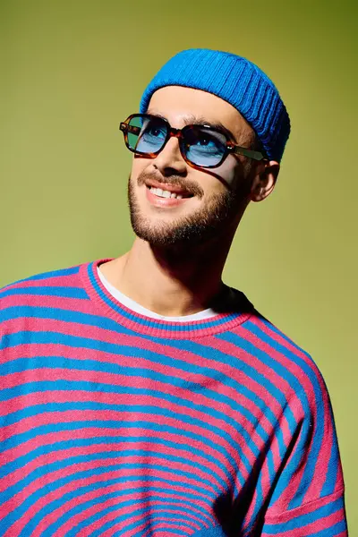 A stylish young man in vibrant sunglasses and a colorful outfit smiles in a chic studio. — Photo de stock