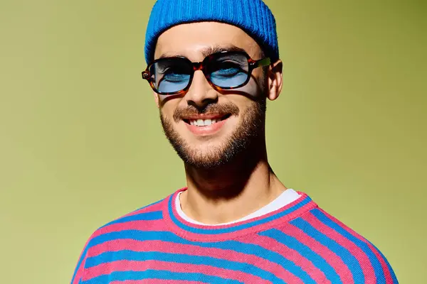 Handsome young man confidently poses in a trendy outfit with vibrant blue sunglasses, exuding style. — Stock Photo