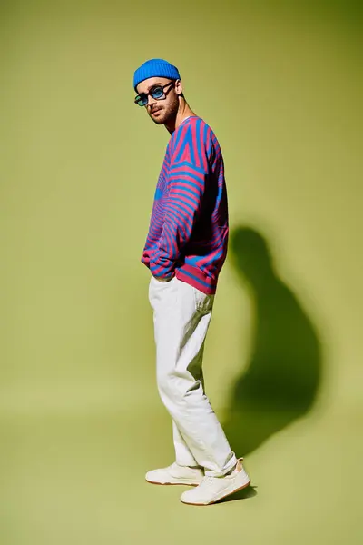 A stylish young man in trendy sunglasses and a colorful outfit stands confidently in green. — Stock Photo
