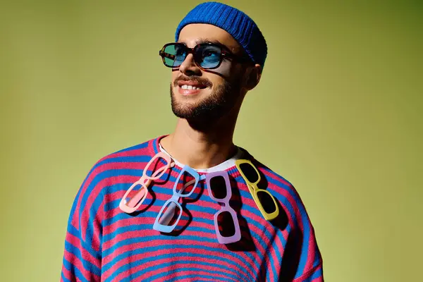 A fashionable young man exhibits his unique style with colorful sunglasses against a green backdrop. — Stock Photo
