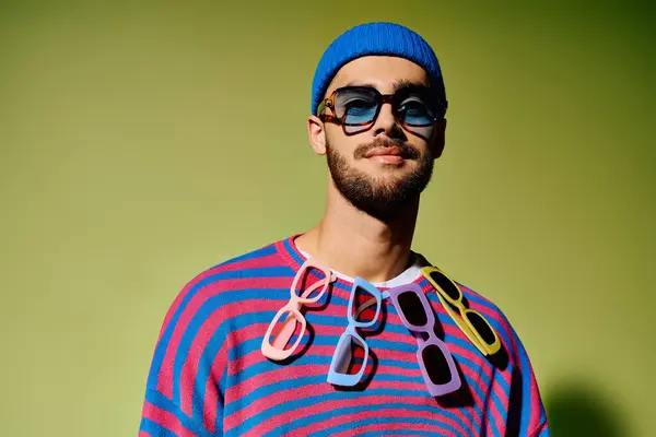 A young man displays his trendy outfit complemented by colorful sunglasses in a studio setting. — Stock Photo