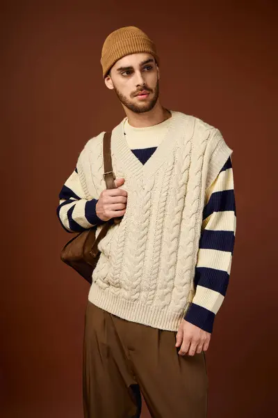 A stylish young man displays his trendy outfit in a studio setting against a brown backdrop. — Stock Photo