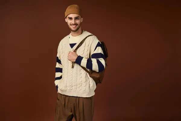 A happy young man in a beanie poses confidently against a warm backdrop. — Stock Photo