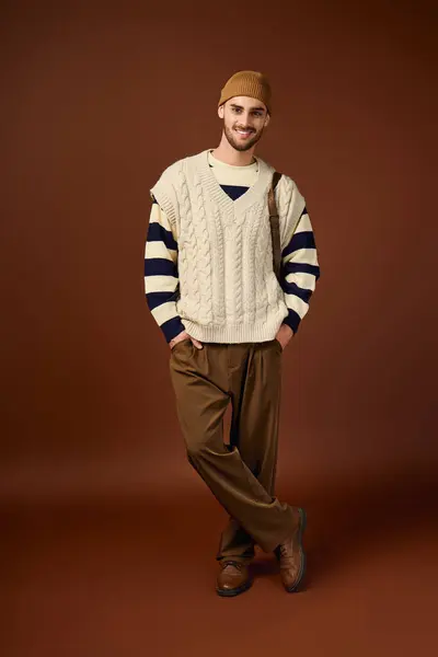 Handsome young man flaunts a chic outfit and trendy beanie hat against a rich brown backdrop. — Stock Photo