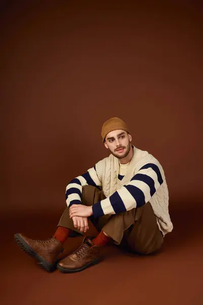 A fashionable young man sits in a studio with a green background, showcasing his trendy style. — Stock Photo