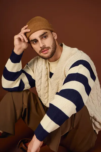 Selbstbewusster junger Mann zeigt in einem Atelier vor braunem Hintergrund seine Wintermode. — Stockfoto