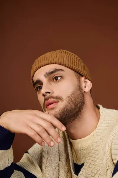 A young man showcases his style with a trendy beanie against a brown backdrop. — Stock Photo