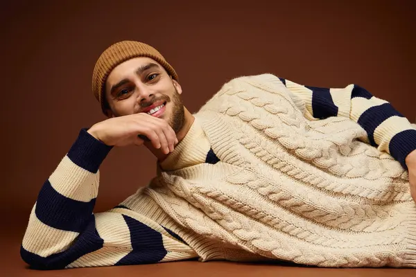 Stylish young man with a beanie displays his bold fashion choices against a brown backdrop. — Stock Photo