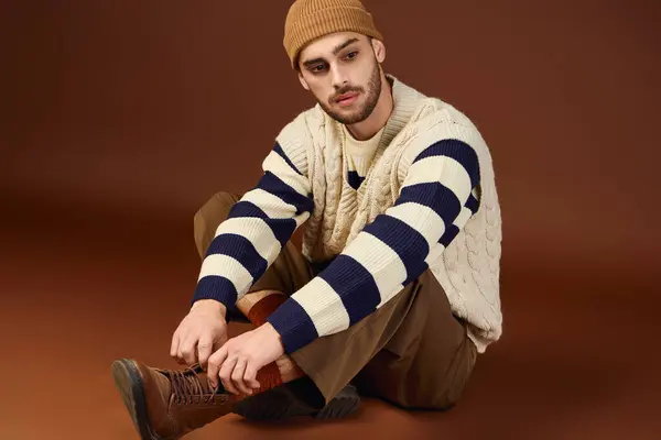 A stylish young man showcases his fashion with a beanie against a brown backdrop. — Stock Photo