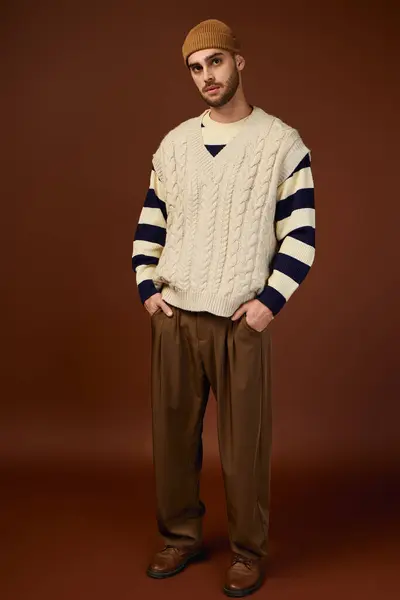 A young man models a stylish winter outfit with a cozy beanie against a warm backdrop. — Stock Photo