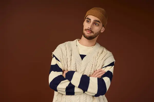 Handsome young man wearing a stylish outfit and beanie poses confidently against a brown background. — Stock Photo