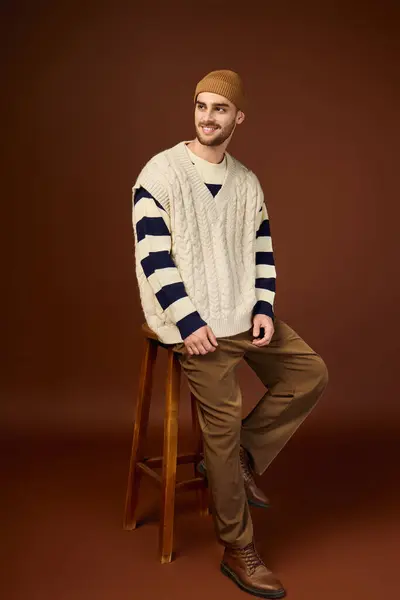 Ein junger Mann posiert in stylischem Strickpullover und Mütze vor brauner Studiokulisse. — Stockfoto