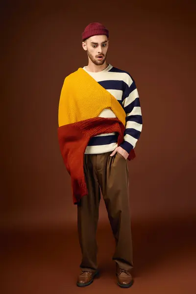 Handsome young man displays a trendy outfit with a beanie against a warm backdrop. — Stock Photo