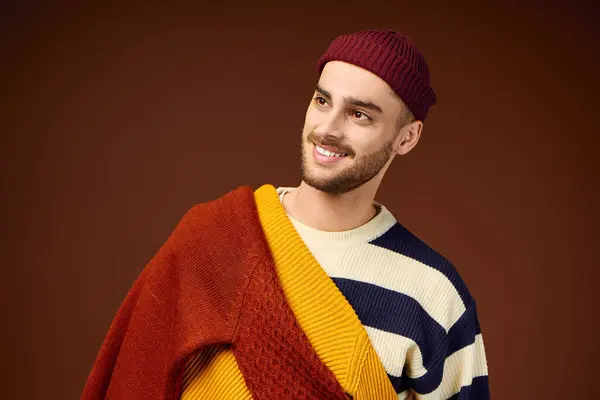 A young man showcases his stylish winter outfit, complete with a trendy beanie hat, in a studio. — Stock Photo