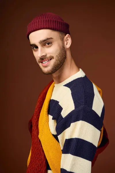 Un joven con estilo en un gorro de moda y ropa vibrante posa en un estudio. - foto de stock
