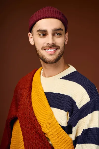 Handsome young man showcases his fashionable outfit and vibrant beanie against a warm backdrop. — Stock Photo