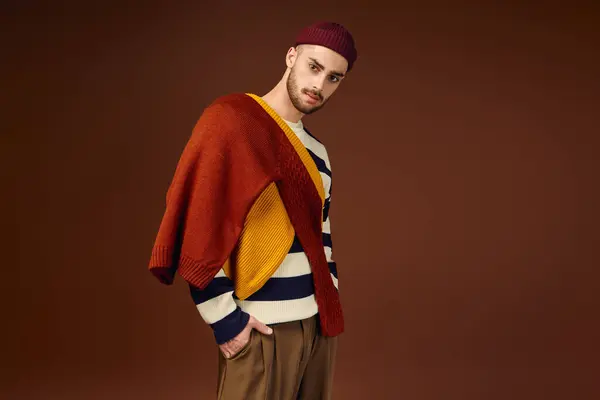 Beau jeune homme affiche tenue à la mode et bonnet chapeau dans une atmosphère de studio dynamique. — Photo de stock
