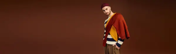 A fashionable young man confidently poses in a studio, flaunting his stylish outfit and beanie. — Stock Photo