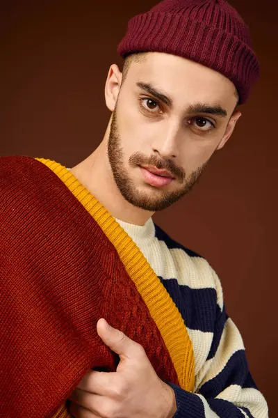 Un jeune homme met en valeur son style unique avec un bonnet et une tenue vibrante sur fond brun. — Photo de stock