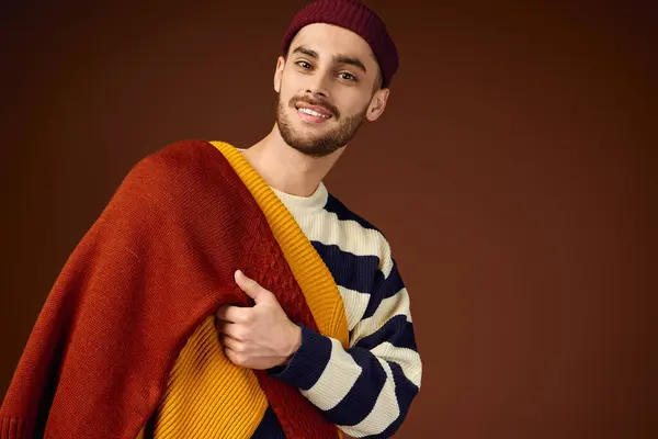 Un joven muestra su estilo en punto en capas y un gorro chic sobre un fondo cálido. - foto de stock